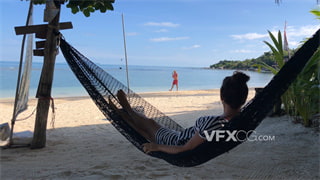 实拍视频女人惬意躺在海滩阴凉处摇晃吊床上享受风景